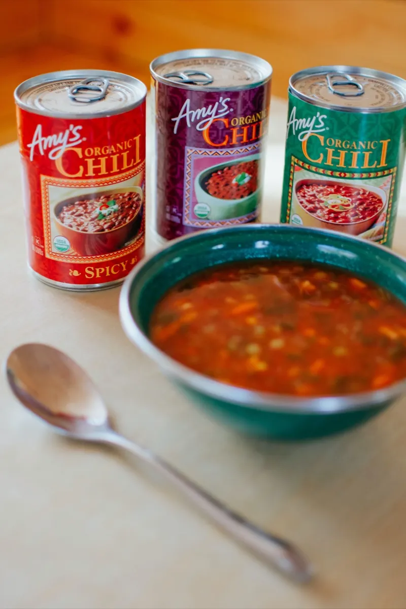 Cans of chili beside a bowl of chili